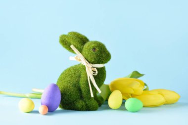 Mavi arka planda yumurtaları ve çiçekleri olan şirin Paskalya tavşanı