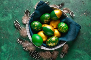 Şık Paskalya yumurtaları ve yeşil arka planda tüyleri olan sepet.