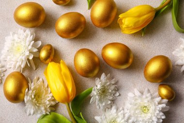 Altın boyalı Paskalya yumurtaları ve çiçekler açık arkaplanda