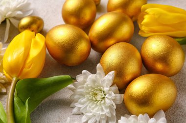 Altın boyalı Paskalya yumurtaları ve çiçekler açık arkaplanda