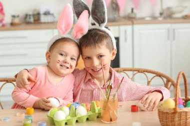 Erkek kardeşiyle birlikte evde paskalya yumurtası boyayan tavşan kulaklı şirin bir kız.