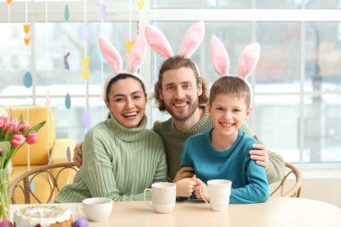 Mutlu ebeveynler ve küçük oğulları tavşan kulakları ile masaya paskalya yumurtası boyuyorlar.