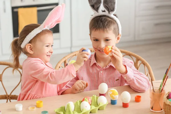 Erkek kardeşiyle birlikte evde paskalya yumurtası boyayan tavşan kulaklı şirin bir kız.