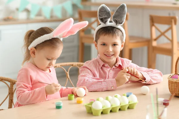 Küçük şirin bir kız ve erkek kardeşi tavşan kulaklı evde paskalya yumurtası boyuyor.