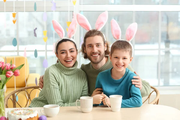 Mutlu ebeveynler ve küçük oğulları tavşan kulakları ile masaya paskalya yumurtası boyuyorlar.