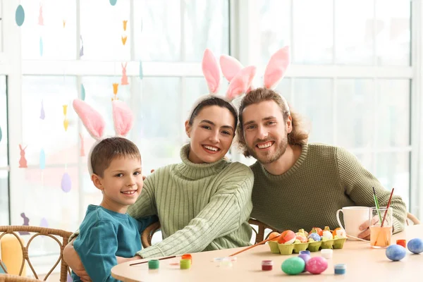 幸せな両親とともに彼らの小さな息子でウサギの耳絵イースターエッグでテーブル — ストック写真