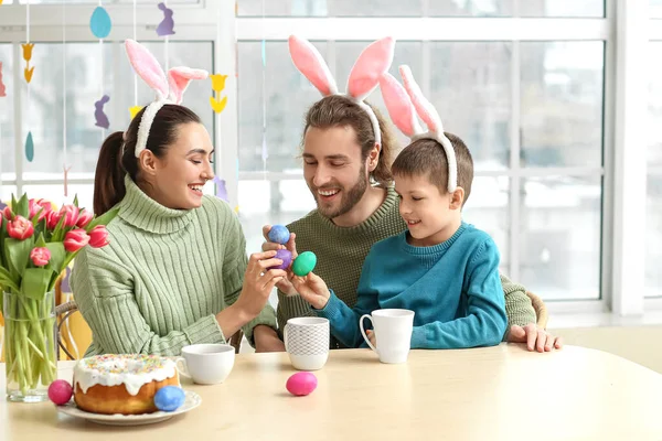幸せな両親とともに彼らの小さな息子でウサギ耳壊すイースターエッグでテーブル — ストック写真