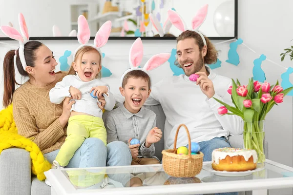幸せな家族でウサギの耳とともにイースターエッグ座っていますソファに家 — ストック写真
