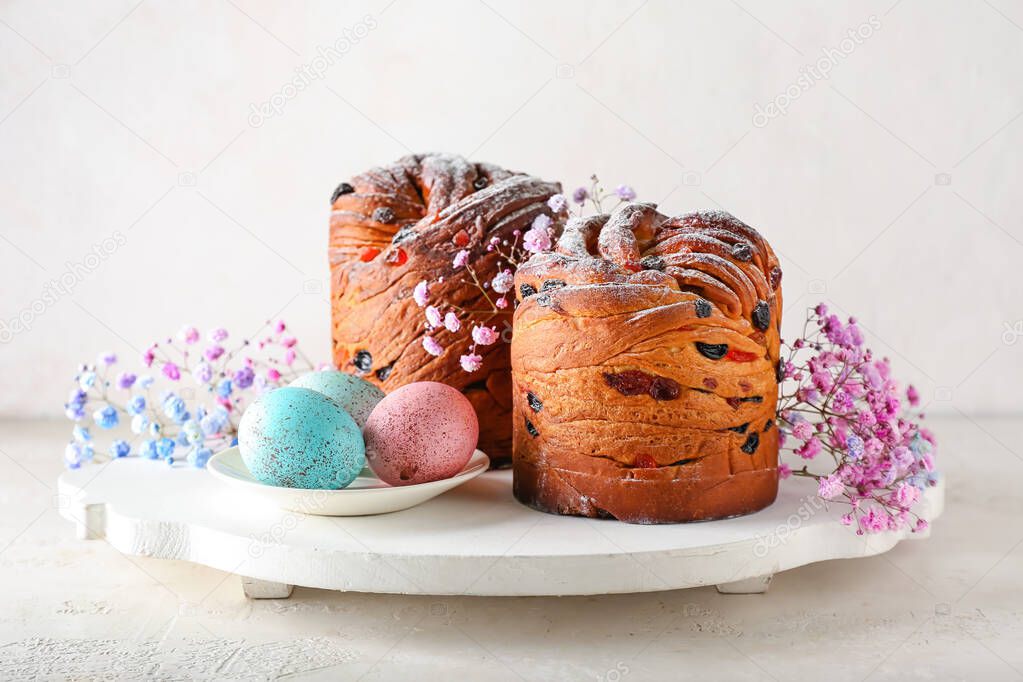 Wooden board with delicious Easter cake, eggs and gypsophila flowers on light background