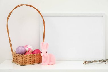 Composition with photo frame, Easter eggs, bunny and pussy willow branches on table near light wall