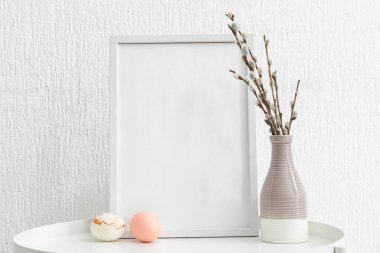 Empty picture frame, Easter eggs and vase with pussy willow branches on table against light background