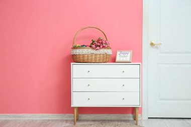 Paskalya yumurtaları ve çiçeklerle dolu Hasır sepet. Odadaki çekmecelerin üzerinde.