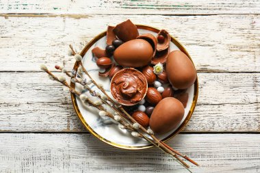 Plate with chocolate Easter eggs and pussy willow branches on light wooden background