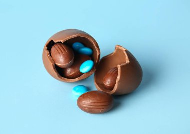 Kırık çikolatalı Paskalya yumurtası ve mavi arka planda şekerler.