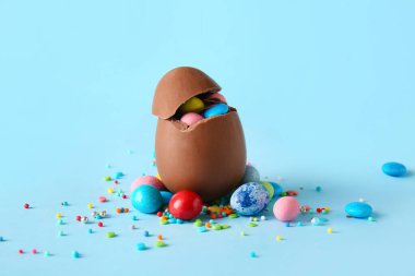 Kırık paskalya yumurtası, mavi arka planda farklı şekerler ve serpiştirilmiş şekerler, yakın plan.