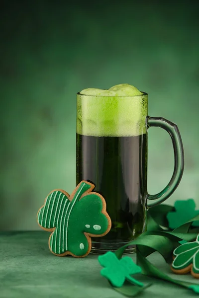Glass of beer and gingerbread cookies in shape of clover leaf on green background. St. Patrick\'s Day celebration
