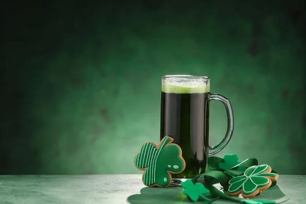 Glass of beer and gingerbread cookies in shape of clover leaf on green background. St. Patrick\'s Day celebration