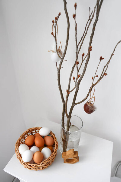 Vase with branches and basket of Easter eggs on table in room