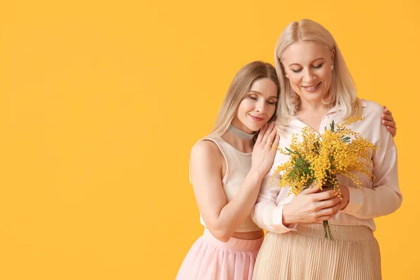 Ung Kvinna Med Sin Mor Och Mimosa Blommor Gul Bakgrund — Stockfoto