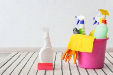 Açık duvarın yanındaki çizgili halıda temizlik malzemeleriyle dolu kova.