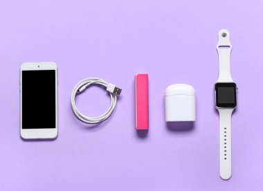 Cep telefonu, USB kablosu, kulaklığı ve eflatun arkaplanlı akıllı bankası.
