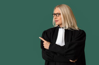 Olgun kadın yargıç yeşil arka plandaki bir şeye işaret ediyor.