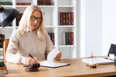 Mahkeme masasında belgelerle çalışan olgun bir kadın yargıç.