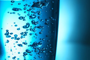 Mavi zemin üzerinde kabarcıklar olan bir bardak berrak su, yakın plan