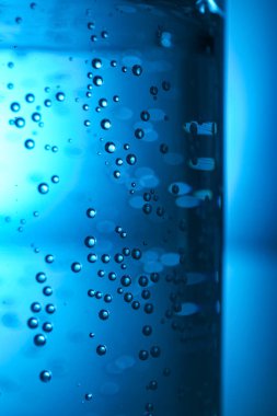 Mavi zemin üzerinde kabarcıklar olan bir bardak berrak su, yakın plan