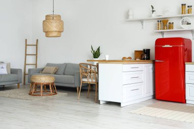 Beyaz tezgahlı, kırmızı buzdolabı ve kanepeli aydınlık mutfağın içi.