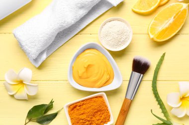 Tabakta zerdeçal maskeli kompozisyon, toz, makyaj fırçası ve renkli ahşap arka planda çiçekler