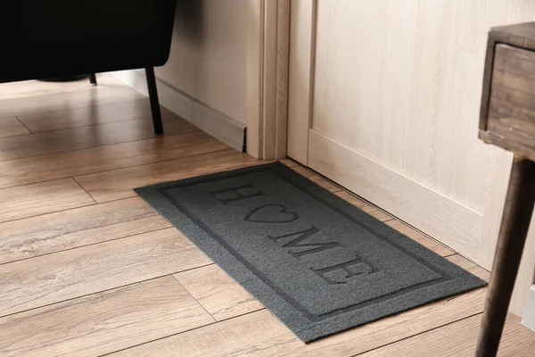 Koridordaki ahşap kapının yanındaki modern paspas. Yakın plan.