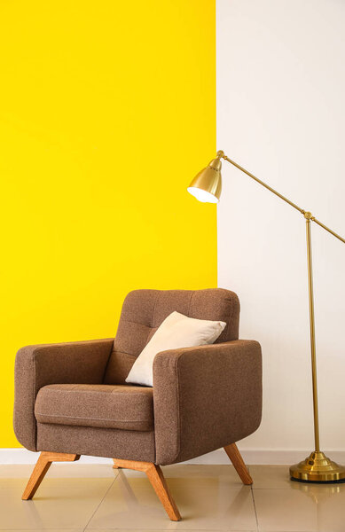 Golden standard lamp and armchair near color wall