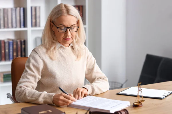 Olgun kadın yargıç mahkeme masasında belge imzalıyor.