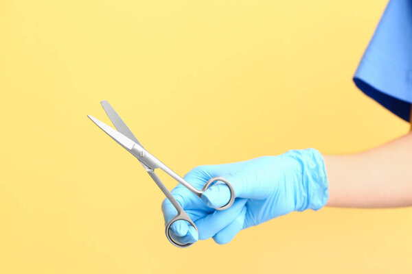 Female doctor with medical scissors on yellow background