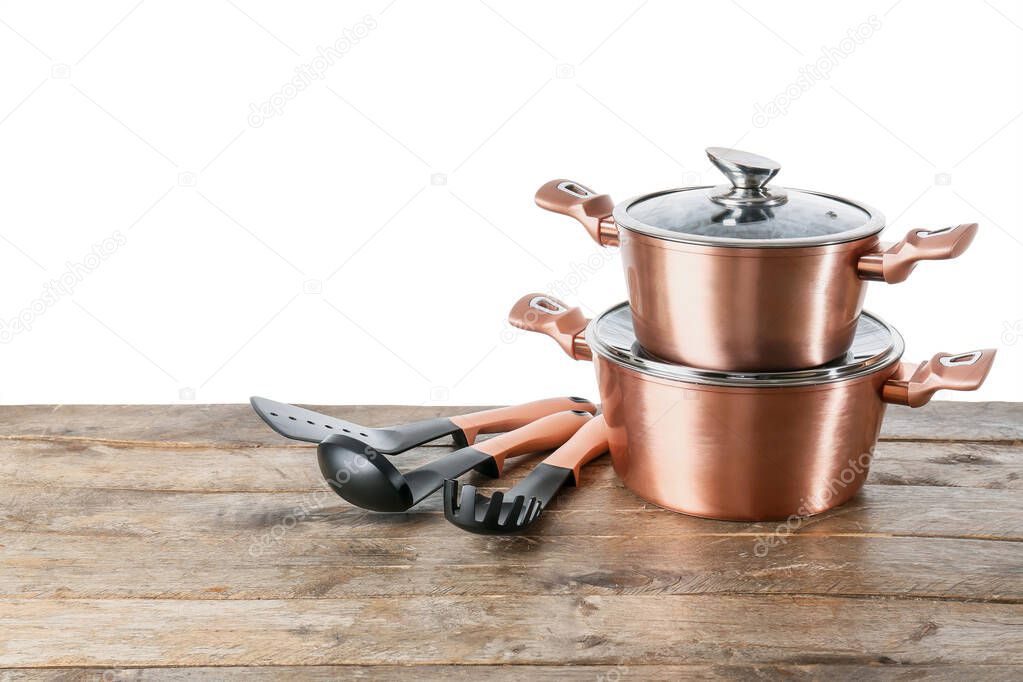 Set of copper kitchen utensils on wooden table against white background