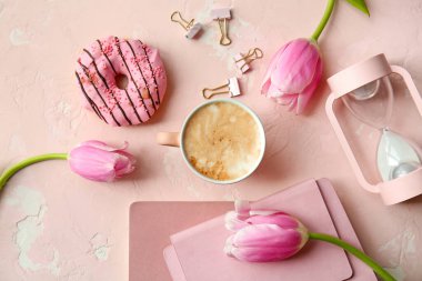 Bir fincan kahve, defterler, çiçekler ve renkli donut.