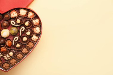 Kalp şeklinde bir kutu, arka planda çikolata şekerleri var.