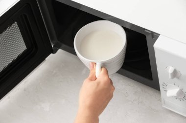 Mikrodalga fırından sütlü fincan alan genç kadın, yakın plan.