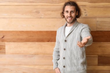 Ahşap arka planda örülü süveter giyen yakışıklı bir genç.