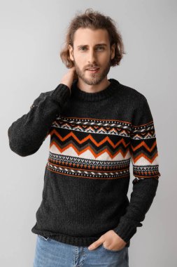 Gri arka planda örülü süveter giyen yakışıklı genç adam.