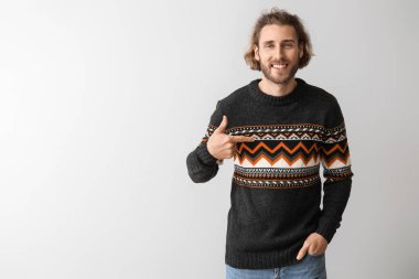 Gri arka planda örülü süveter giyen yakışıklı genç adam.