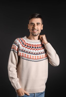 Esmer arka planda örülü süveter giyen yakışıklı bir genç.