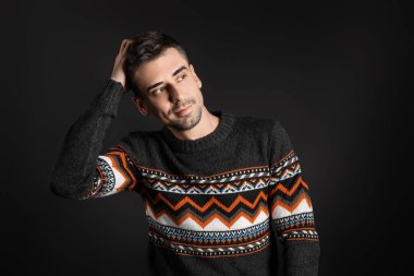 Esmer arka planda örülü süveter giyen yakışıklı bir genç.