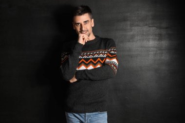 Esmer arka planda örülü süveter giyen yakışıklı bir genç.