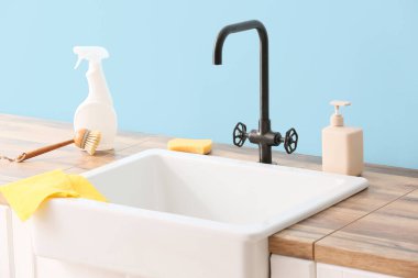 Seramik lavabo ve temizlik malzemeleri mavi duvarın yanında.