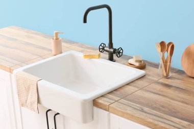 Seramik lavabo ve mutfak malzemeleri mavi duvarın yanında.