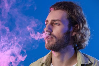 Mavi arka planda sigara içen genç adam