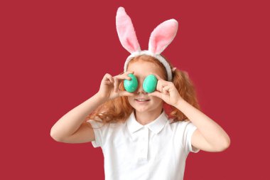 Kırmızı arka planda tavşan kulaklı ve Paskalya yumurtaları olan komik küçük bir kız.