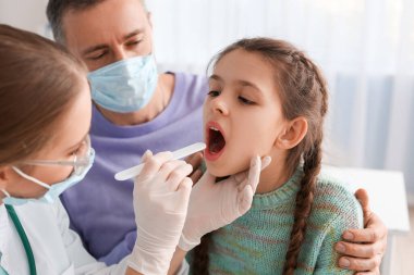 Doktor klinikte boğazı ağrıyan küçük bir kızı muayene ediyor.
